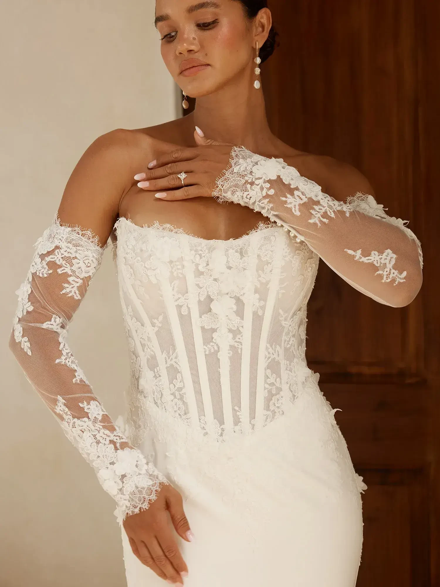 A woman in a white wedding dress with lace details and long sheer sleeves, posing elegantly.