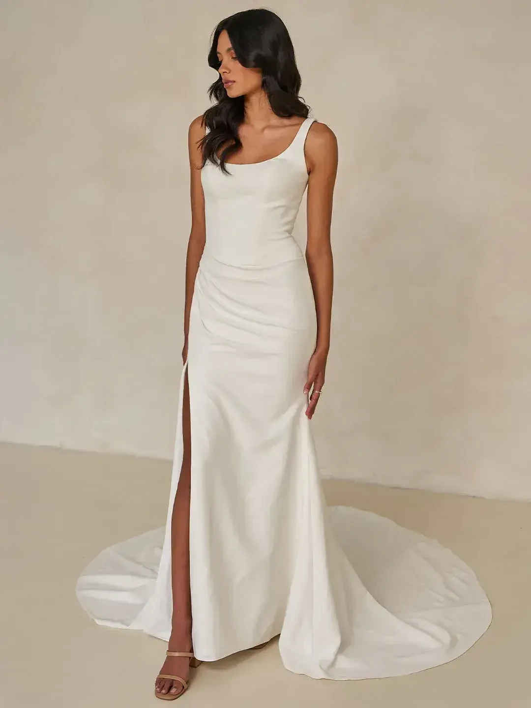 A model wearing a sleek white gown with a thigh-high slit, standing against a neutral background.