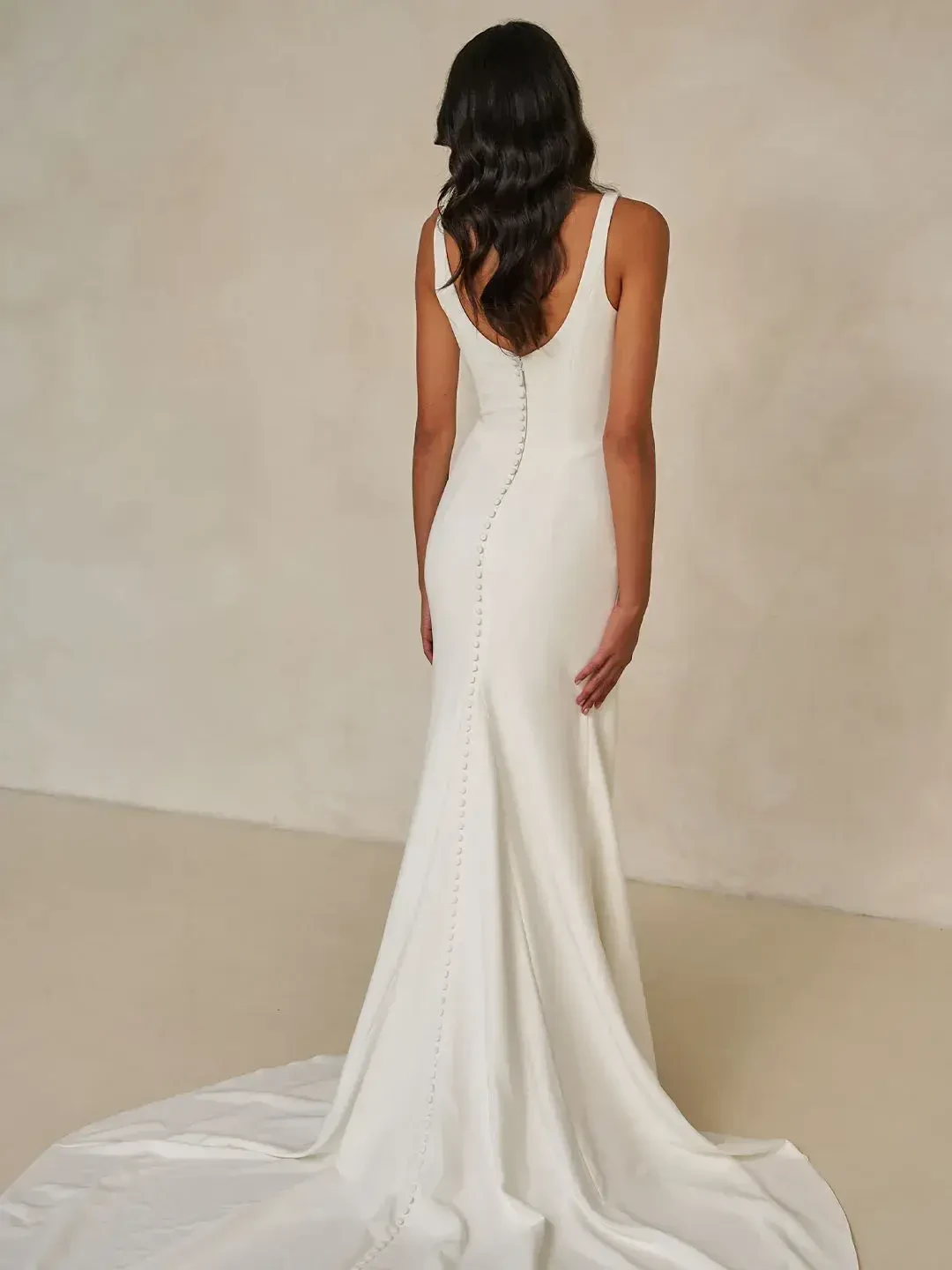 A woman in a white gown, viewed from the back, showcasing a fitted silhouette and a long train.