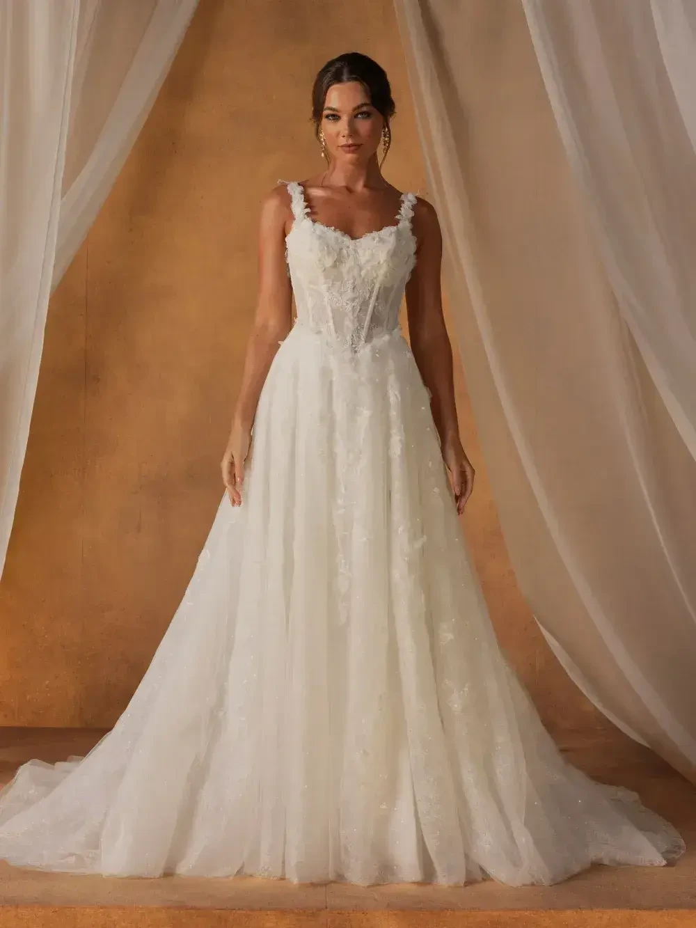 A woman in a white wedding dress with a fitted bodice and flowing skirt, standing against a softly draped background.